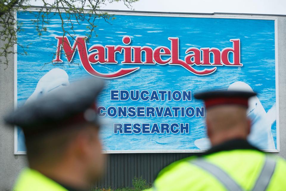 Two police officers in uniform stand in front of a Marineland sign, partially obscured by their backs.