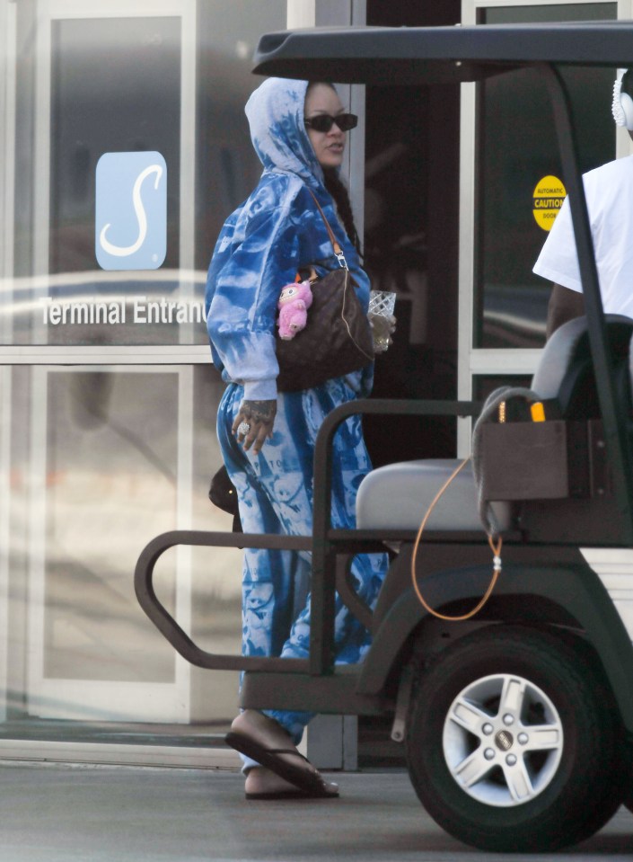 Rihanna in a blue sweatsuit carrying a Louis Vuitton bag after returning from a Caribbean vacation.