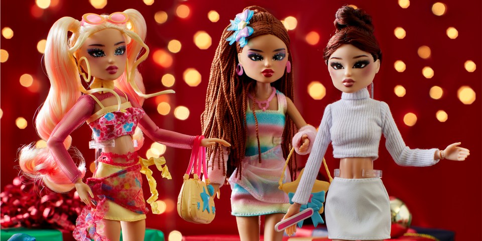 Three fashion dolls in front of a red background with blurred lights.