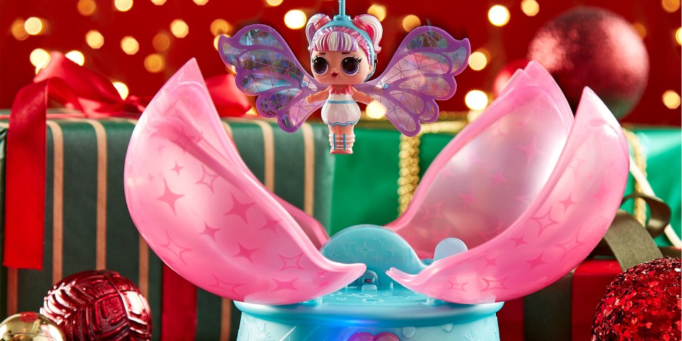 LOL Surprise Magic Flyers toy with wings hovering above a blue and pink opening case, against a background of Christmas decorations.