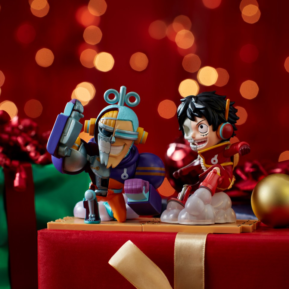 Two action figures, one a robot and one a person with a visible skull, on a red background with bokeh lights, on top of Christmas gifts.
