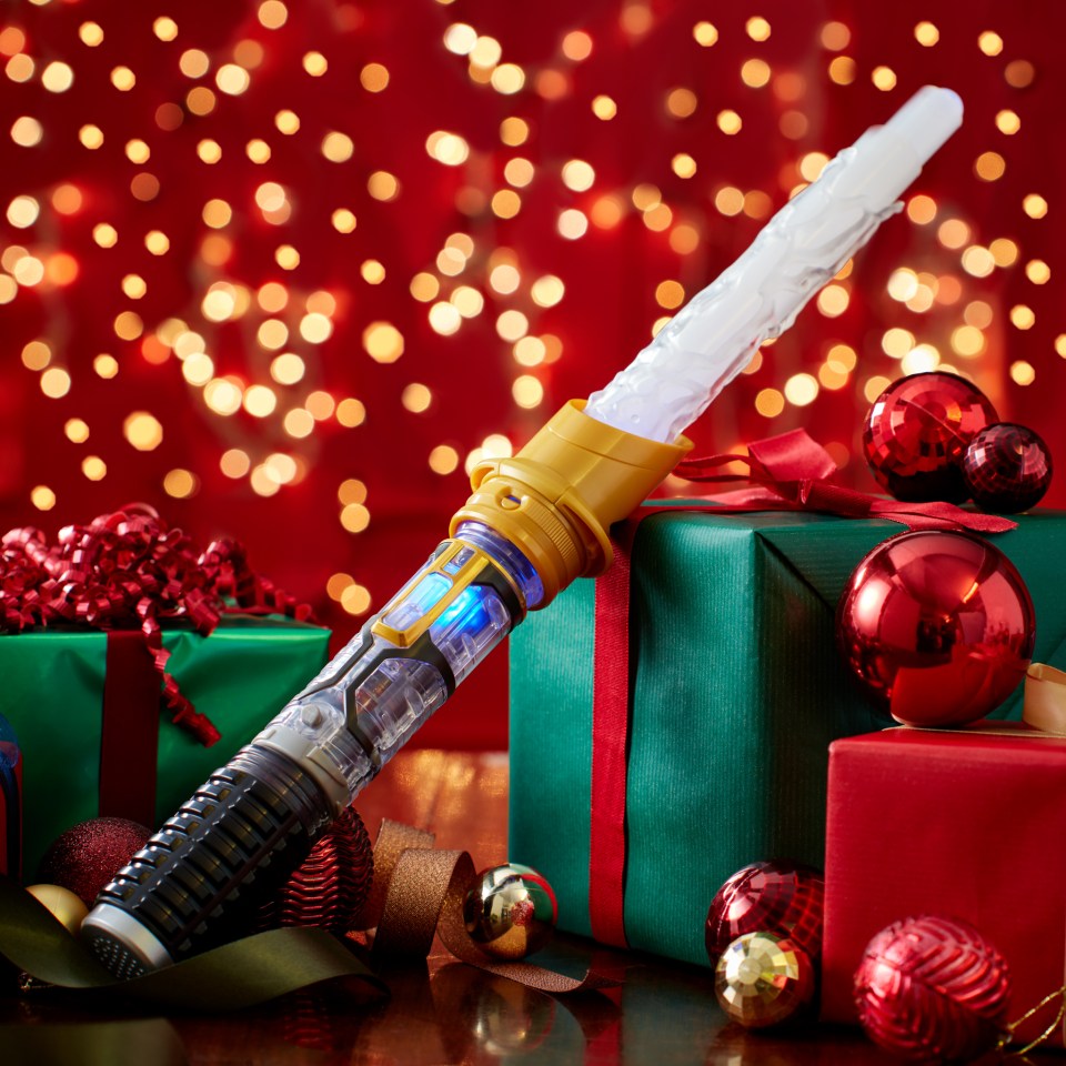 A toy lightsaber with a blue light on a table with Christmas presents and ornaments.