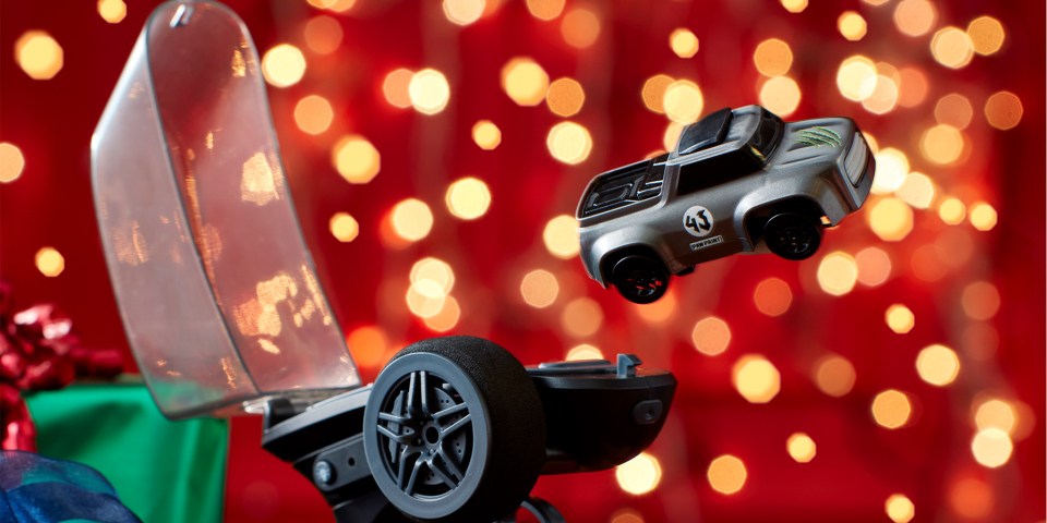 A gray toy car hovering over a launcher against a bokeh red background.