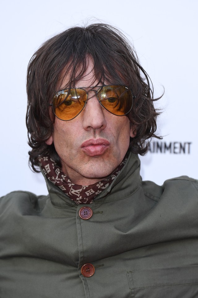Richard Ashcroft wearing amber aviator sunglasses and a brown patterned scarf.