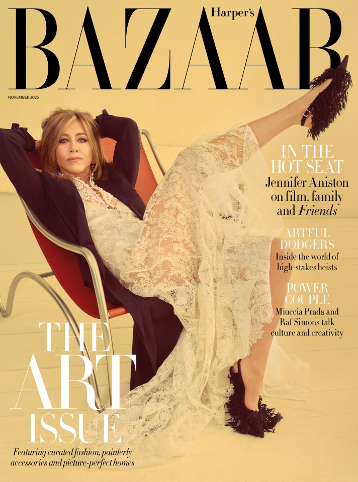 Harper's Bazaar UK November 2025 cover featuring Jennifer Aniston in a black jacket and white lace dress, sitting in a red chair with one leg extended upwards, wearing a black fringed shoe.