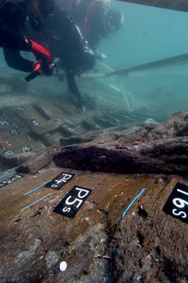Underwater view of a diver examining the timbers of an ancient Roman shipwreck with labeled planks.