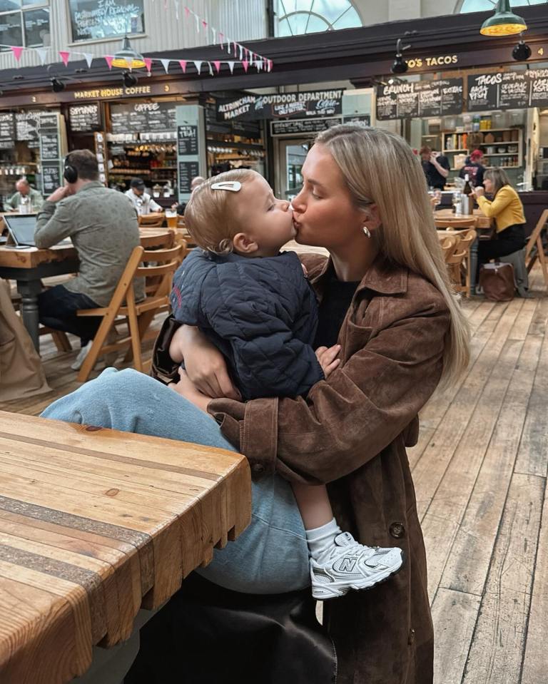 a woman holding a baby in front of a sign that says ' o 's tacos '