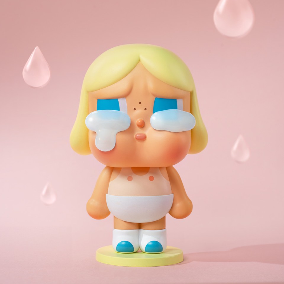Illustration of a Cry Baby toy with blonde hair, wearing a diaper, crying big tears, on a pink background with floating tears.