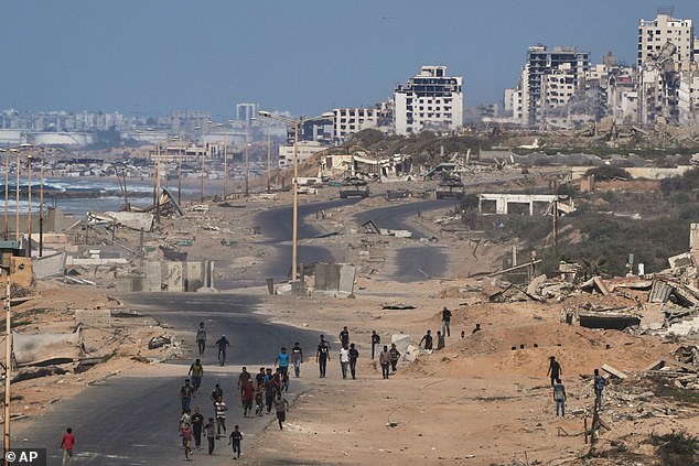 Israeli tanks block the beach road to Gaza City as displaced Palestinians gather on the coastal road near Wadi Gaza after the announcement that Israel and Hamas had agreed to the first phase of a peace plan to pause the fighting, in the central Gaza Strip, Thursday, Oct. 9, 2025