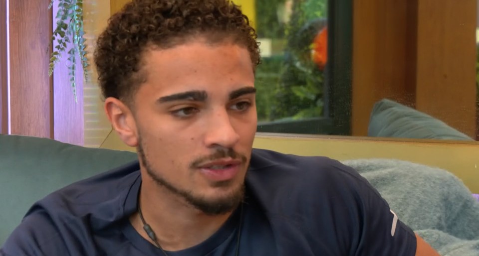 Big Brother contestant Marcus looking confused, with one hand on his curly hair.