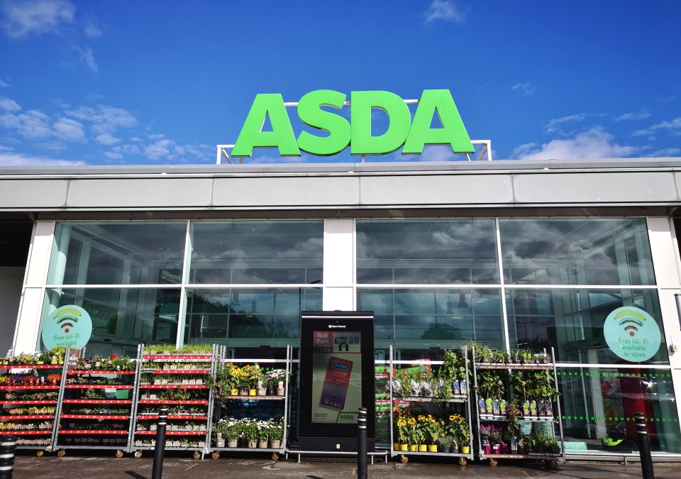 Asda supermarket with a large green "ASDA" sign above its glass storefront and racks of plants and an advertising display outside.