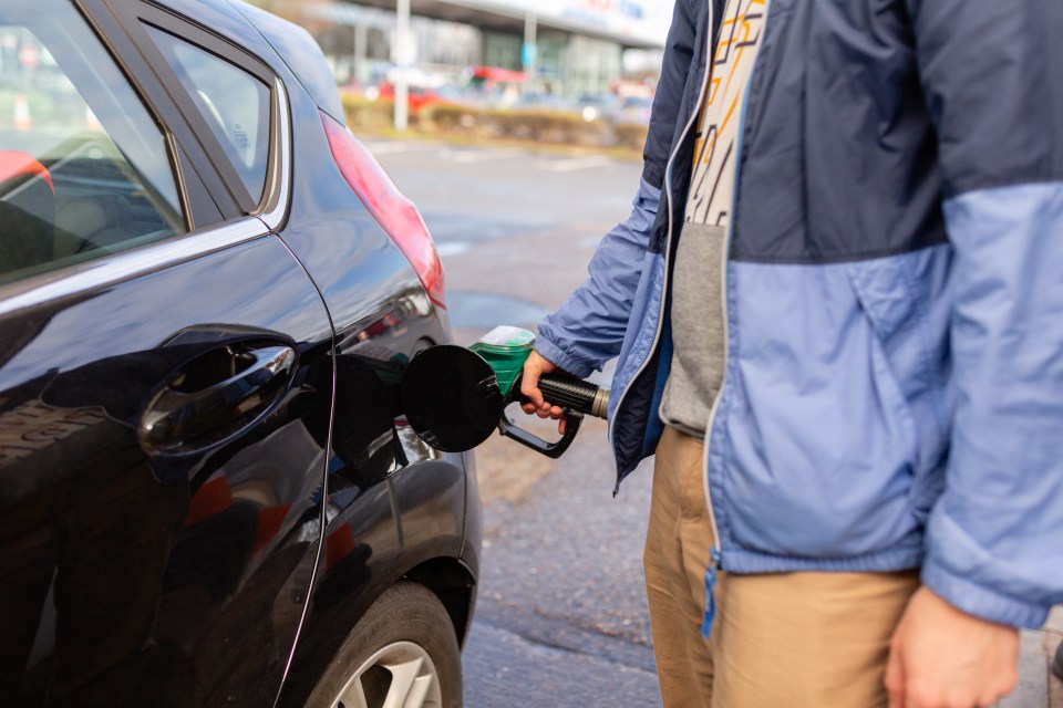 Man holding a petrol pump, filling car at a gas station.