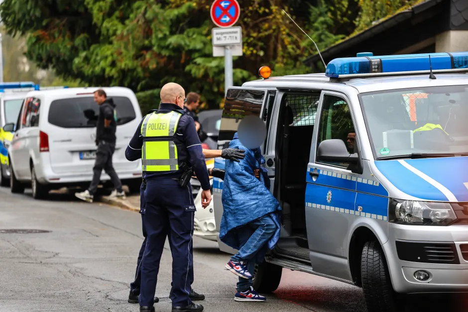Police officers assisting a person with a blue blanket into a police van.