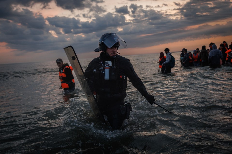 French police officer wading through water to stop migrants boarding boats.
