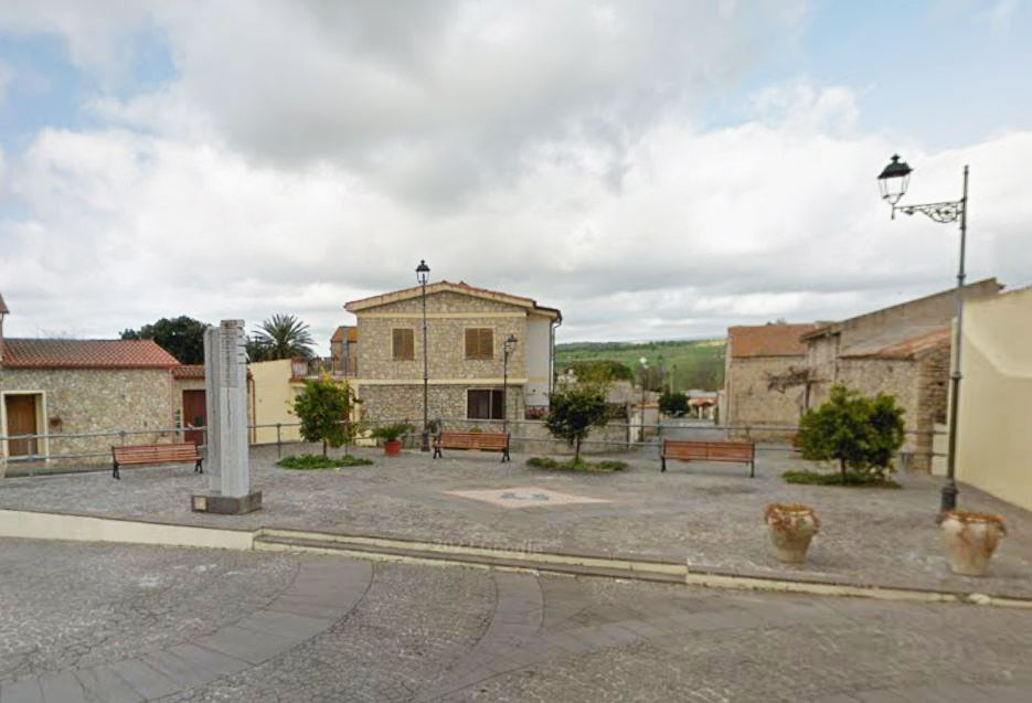 Baradili, Sardinia's smallest village, featuring a central square with benches, trees, and stone buildings.