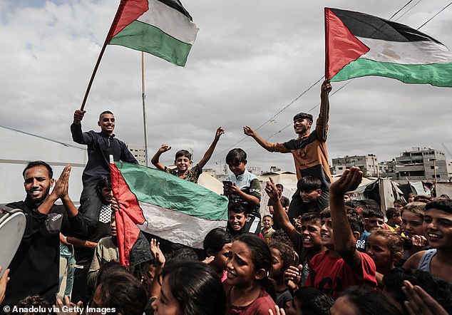 Palestinians gathered at the Nuseirat refugee camp celebrate with flags in Deir al-Balah, Gaza, on October 9, 2025