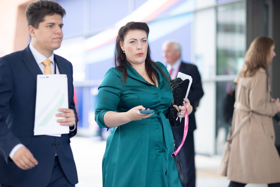 Alicia Kearns MP in a green dress holding a phone and bag, with a matching phone case, during the Conservative Party Conference.