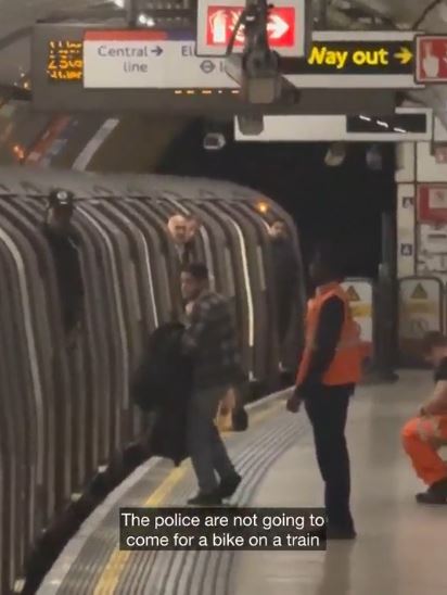 A man holding a bike arguing with train staff on a platform.