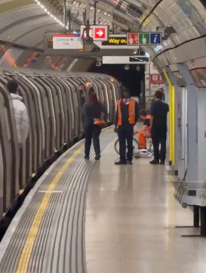 People gathered on a subway platform next to a train, with a cyclist and their bike on the ground.