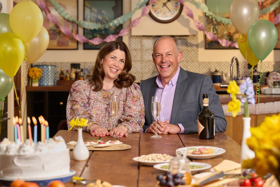 Kirstie Allsopp and Phil Spencer smiling at a table with cake and champagne, celebrating 25 years of Location, Location, Location.