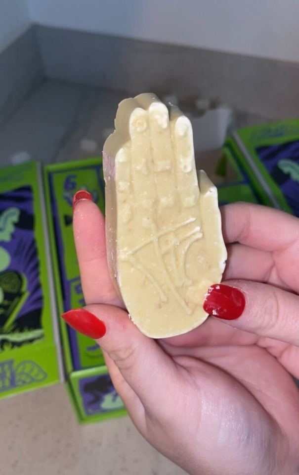 A hand holding a white soap bar shaped like a palm with a symbol carved into it.