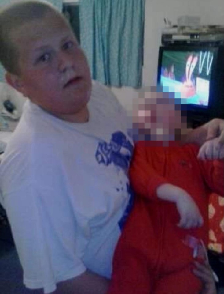 A young person in a white t-shirt holding a child in a red jumpsuit.