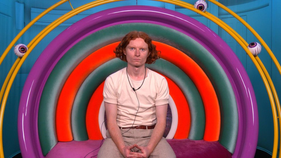 George warning on a set with a rainbow-colored chair and eyeballs.