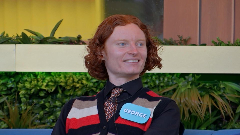George, a young man with red hair, smiles while wearing a patterned tie and a striped cardigan.