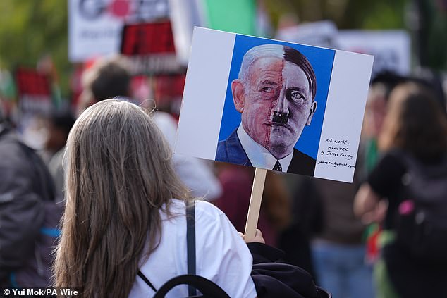 A protester holds a sign depicting two halves of a face - one is Israeli Prime Minister Benjamin Netanyahu, the other is Adolf Hitler