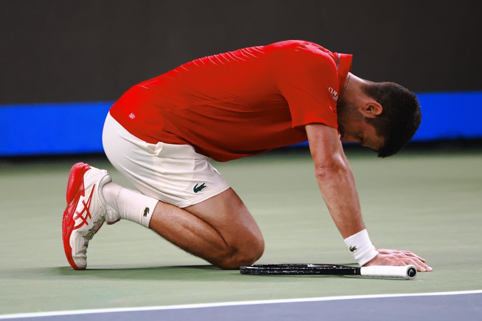 Novak Djokovic on his knees with his head down during a tennis match.