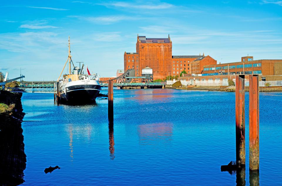 The River Freshney and Corporation Bridge in Grimsby, Lincolnshire, England, with a boat docked nearby and industrial buildings in the background.