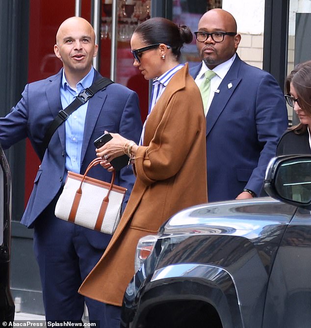 The Duchess of Sussex wore wide-leg navy trousers, paired with a striped blouse and a brown coat while heading to the members club in Manhattan's Meatpacking District