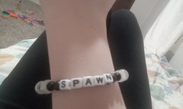Close-up of a person's arm wearing a "SPAWN" beaded bracelet.