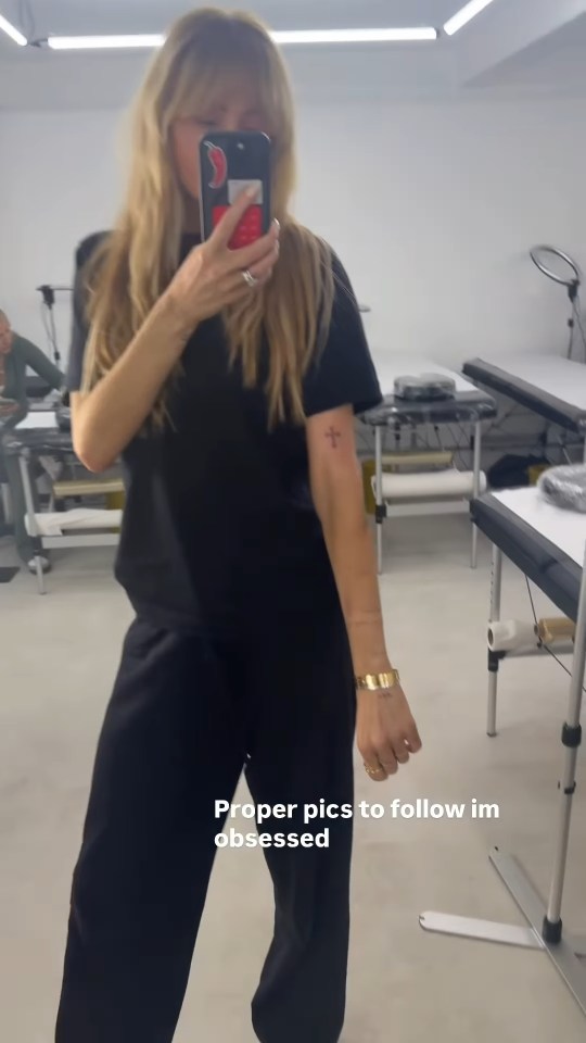 Olivia Attwood posing in a tattoo studio, showing off a new cross tattoo on her right arm.