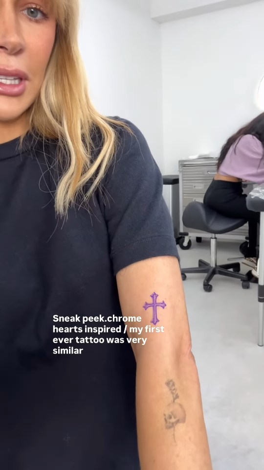 A woman showing a new purple cross tattoo on her right arm.