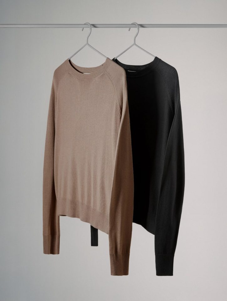 Two sweaters, one tan and one black, hanging on a clothing rack.