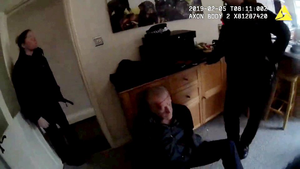 Bodycam footage showing a man sitting on the floor with two police officers standing over him.