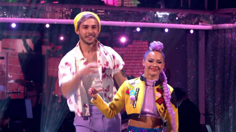 A male dancer with a yellow beanie and an open floral shirt, next to a female dancer with purple hair and a yellow bomber jacket.