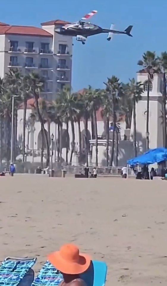 A helicopter flying over a building with palm trees.