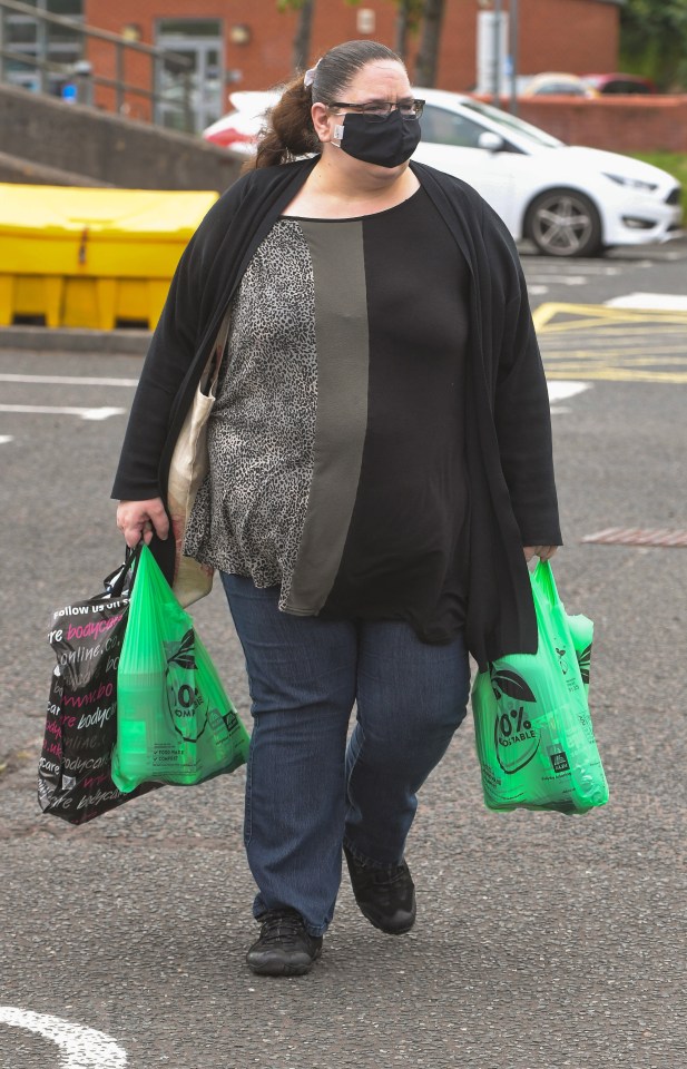 A woman in a face mask, glasses, and dark clothing carries shopping bags.