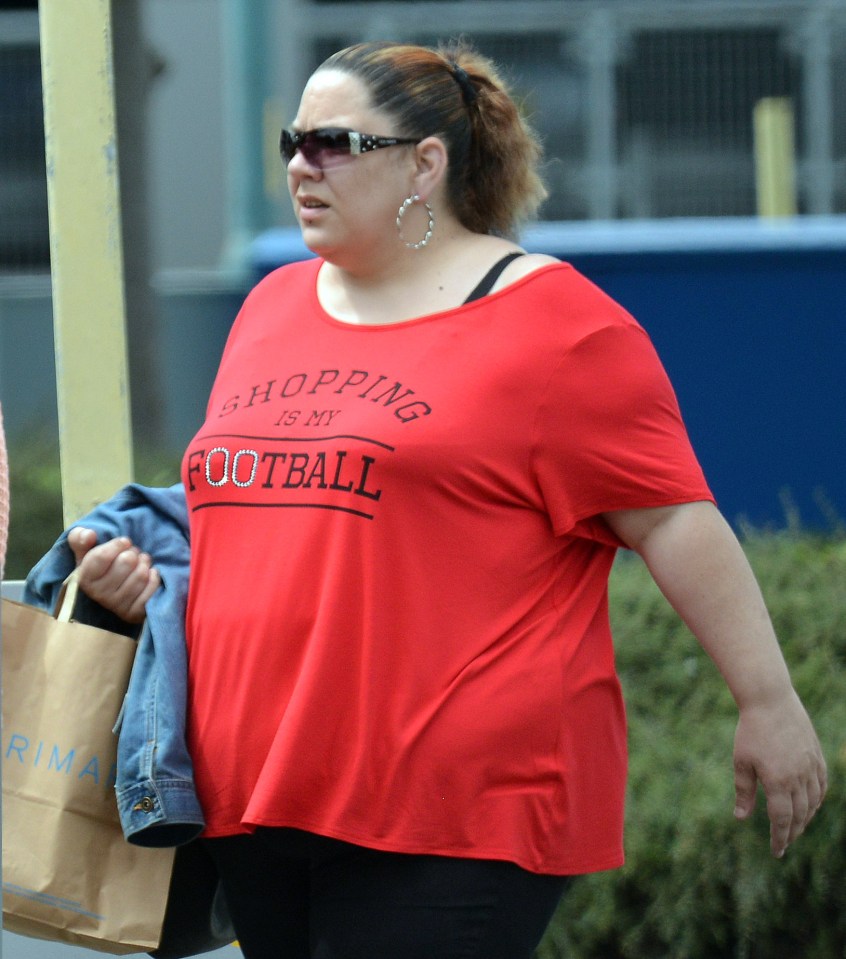 Tracey Connelly wearing a red "SHOPPING IS MY FOOTBALL" t-shirt, carrying a shopping bag and a denim jacket.