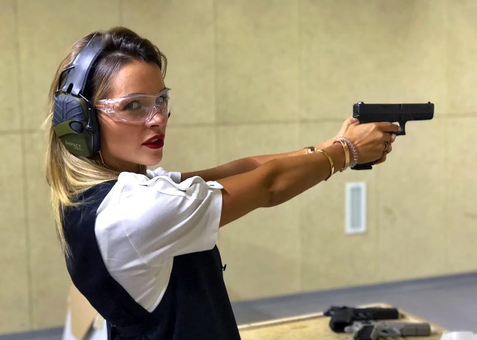 Ksenia Lugovoya at a gun range wearing eye protection and ear defenders while holding a handgun.
