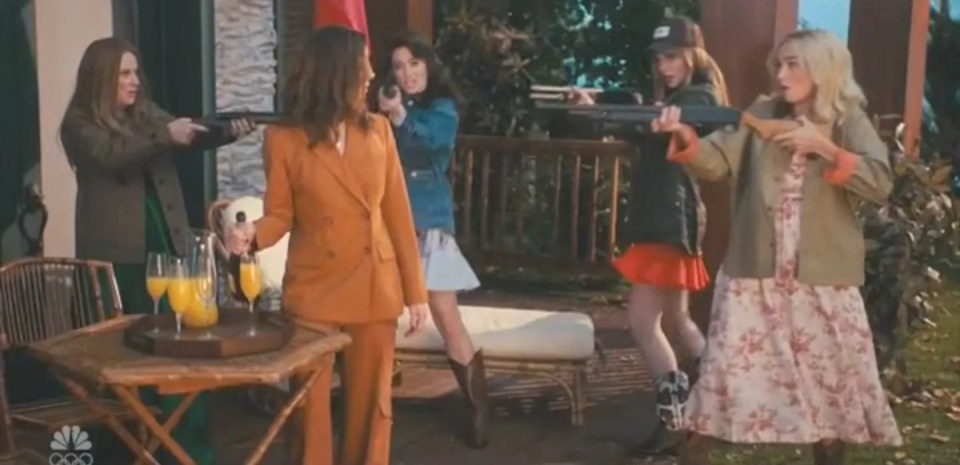A scene from SNL featuring five women aiming shotguns in a comedic manner, with a mimosa set on a table in the foreground.