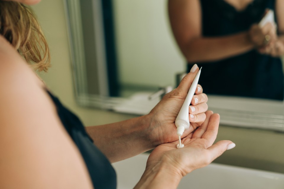 A woman squeezes lotion from a white tube onto her hand.