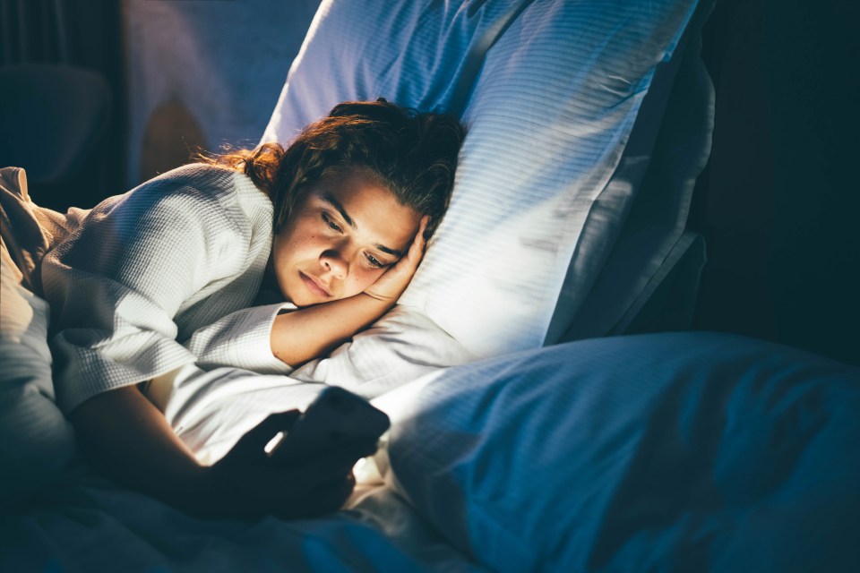 Young woman laying in bed using a smart phone.