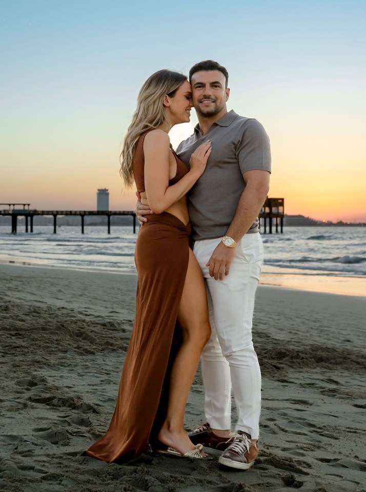 Vicky Pattison and Ercan Ram embracing on a beach with a sunset and pier in the background.