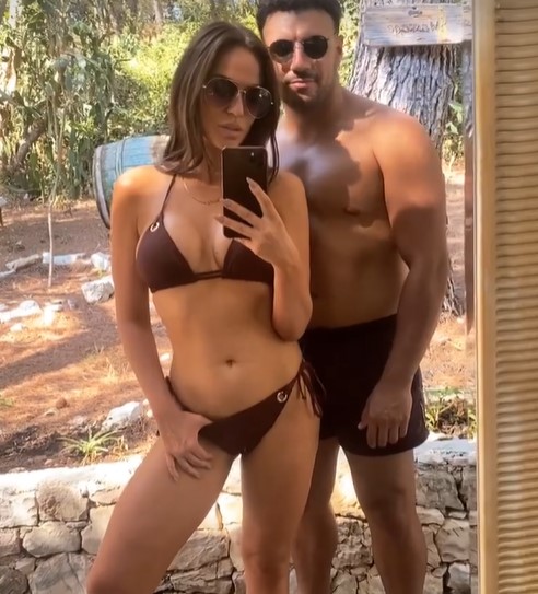 Vicky Pattison takes a mirror selfie in a brown bikini with her boyfriend Ercan in swim trunks standing behind her.