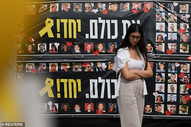 A woman is seen walking past a banner filled with faces of hostages who were kidnapped during the horrid October 7, 2023 attack following the ceasefire
