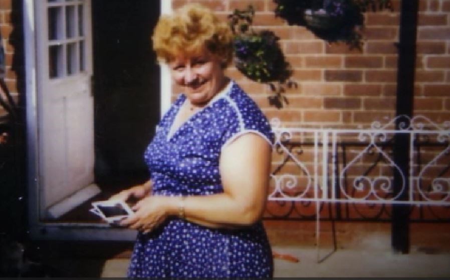 Nora Tait, a woman with blonde hair, wearing a red floral top.