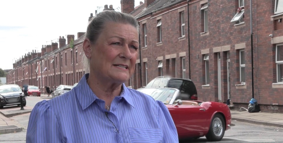 A woman speaks about the horrific way her parents were taken, standing in front of terraced houses and a red convertible car.